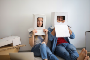 Lustige Tipps für die Ehe: Paar mit Kisten auf dem Kopf sitzt beim Umzug im Wohnzimmer und hat Spaß